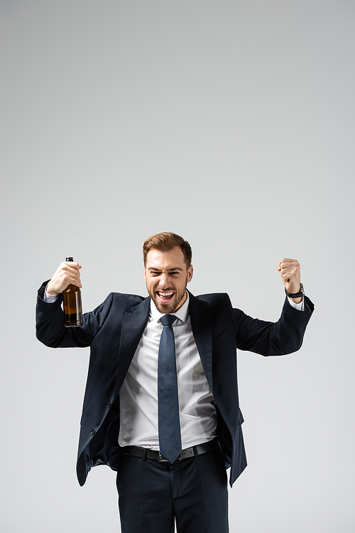 handsome businessman in suit rejoicing with beer isolated on grey