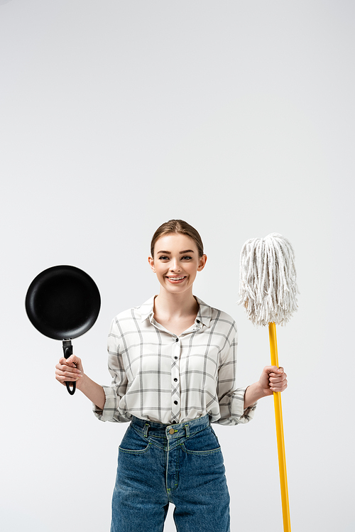 smiling girl posing like puppet with mop and frying pan isolated on grey
