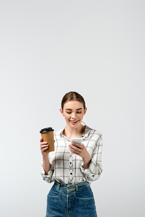 smiling attractive girl using smartphone and holding paper cup isolated on grey