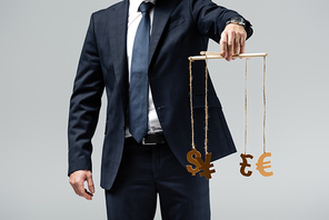 cropped view of puppeteer in suit holding currency signs on strings isolated on grey