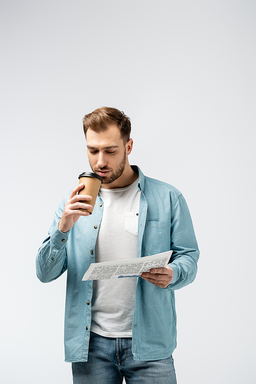 young man reading newspaper and drinking coffee isolated on grey