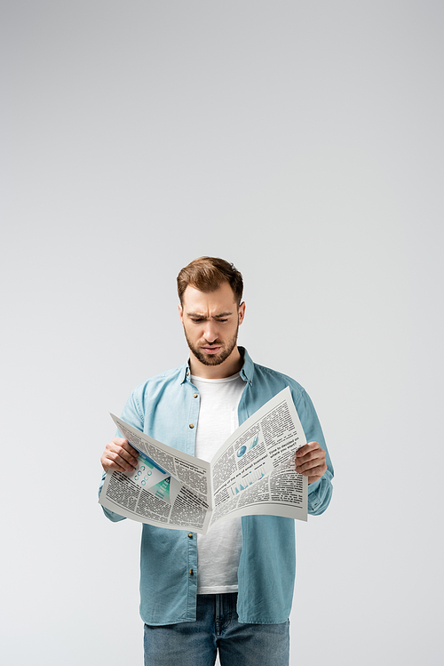confused young man reading newspaper isolated on grey