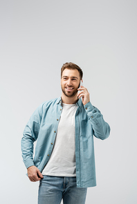 smiling young man talking on smartphone isolated on grey