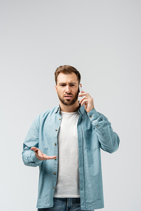 confused young man talking on smartphone isolated on grey