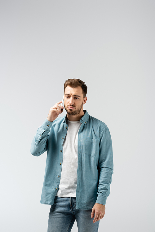 sad young man talking on smartphone isolated on grey