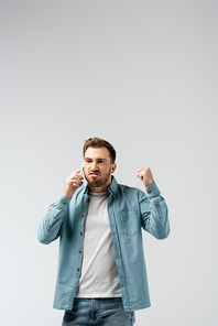 angry young man talking on smartphone and showing fist isolated on grey