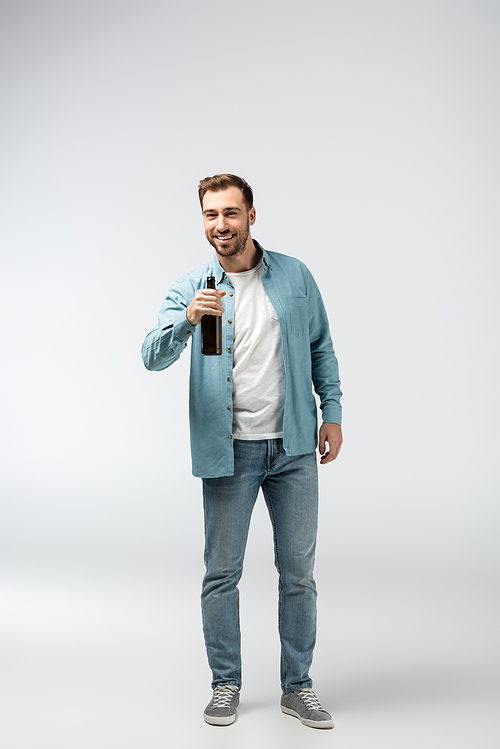 smiling young man with bottle of beer isolated on grey