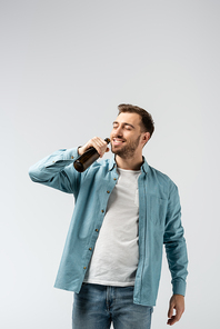 smiling young man drinking beer from bottle isolated on grey
