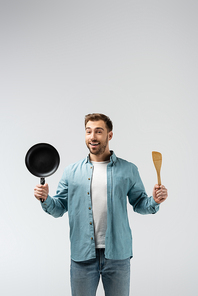 happy young man with frying pan and spatula isolated on grey