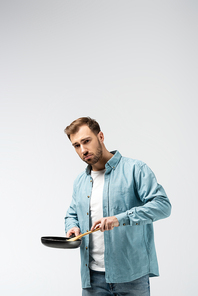 sad young man with frying pan and spatula isolated on grey