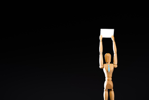 wooden marionette in tie holding blank placard isolated on black