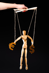 cropped view of puppeteer holding wooden marionette on strings with currency signs isolated on black