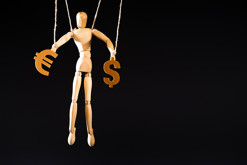 wooden marionette on strings holding currency signs isolated on black