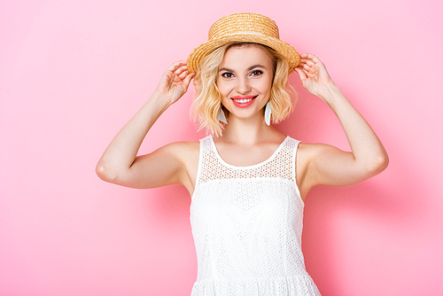 young woman in white dress touching straw hat on pink