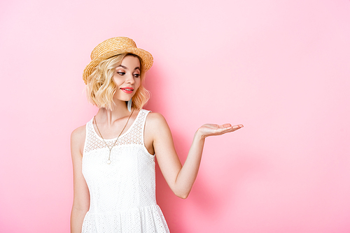 young woman in straw hat and dress pointing with hand on pink