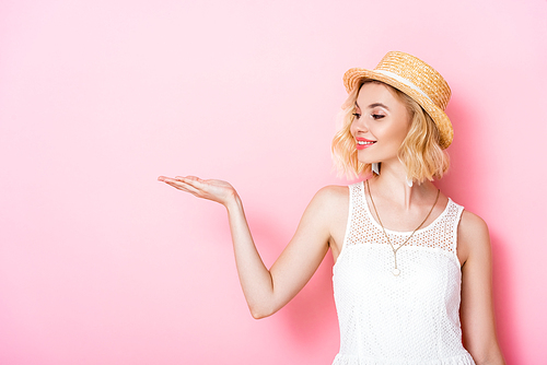 young woman in straw hat and dress pointing with hand on pink