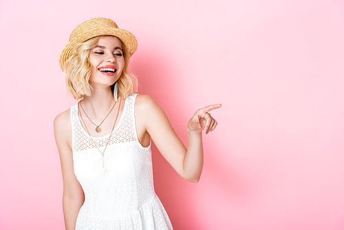 woman in straw hat laughing and pointing with finger on pink