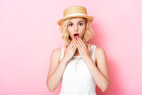 shocked young woman in straw hat covering mouth on pink