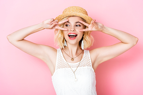 young woman in straw hat showing peace sign on pink