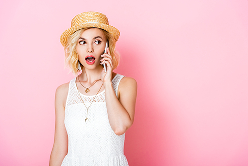 shocked woman in straw hat talking on smartphone on pink