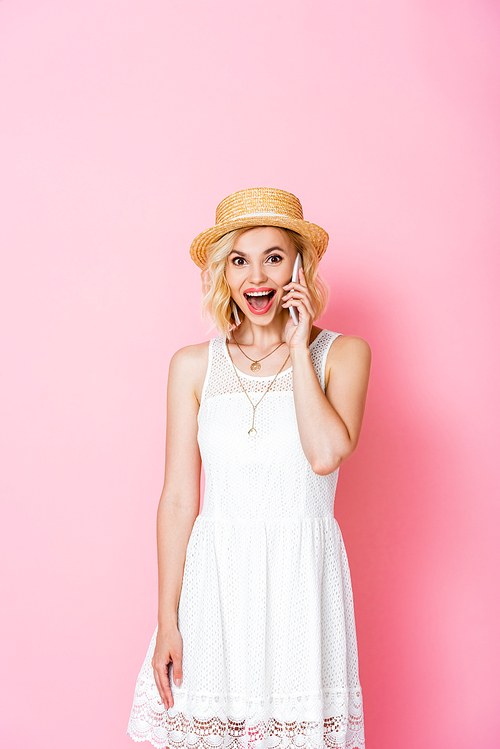 excited woman in straw hat talking on smartphone on pink