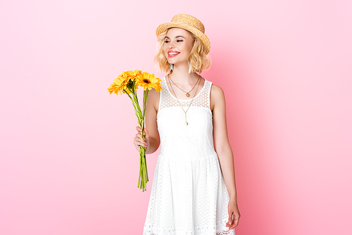 woman in straw hat and white dress holding yellow flowers on pink
