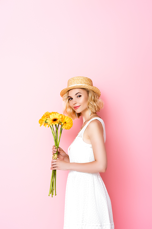 young woman in straw hat and dress holding yellow flowers on pink