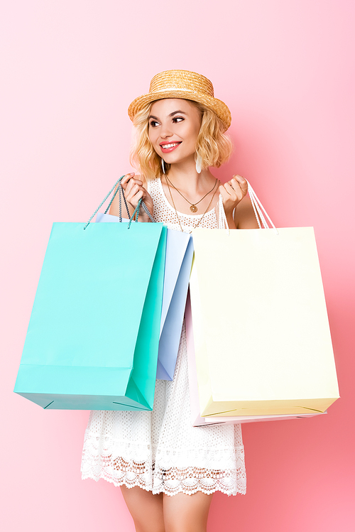 woman in straw hat and dress holding shopping bags on pink