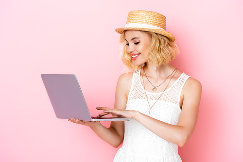 young woman in straw hat using laptop on pink