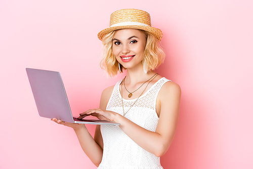 woman in straw hat using laptop on pink