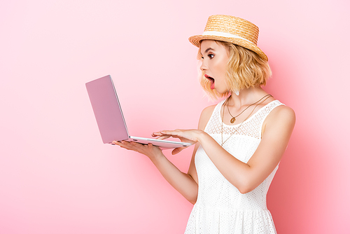 shocked woman in straw hat looking at laptop on pink