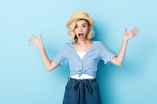shocked young woman in straw hat gesturing on blue