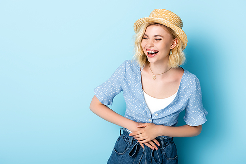 woman in straw hat laughing and touching belly on blue