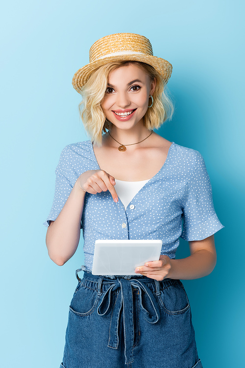 young woman in straw hat pointing with finger at digital tablet on blue