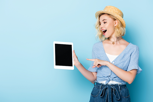 young excited woman pointing with finger at digital tablet with blank screen on blue