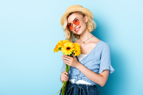woman in straw hat and sunglasses holding flowers on blue