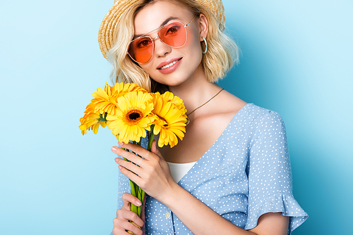 woman in straw hat and sunglasses holding yellow flowers on blue