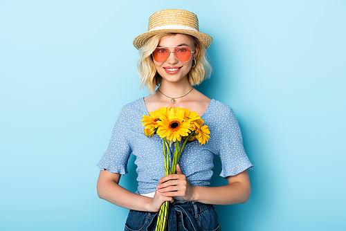 woman in straw hat and sunglasses holding flowers on blue
