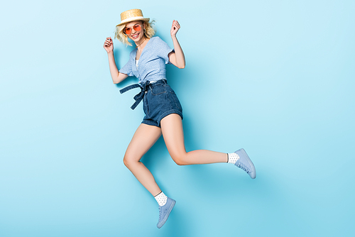 woman in straw hat and sunglasses jumping on blue