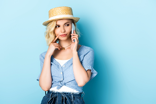 woman in straw hat looking away and talking on smartphone on blue