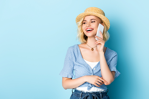 woman in straw hat with open mouth talking on smartphone on blue