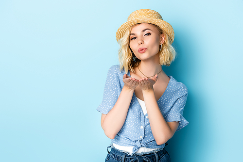 young woman in straw hat sending air kiss on blue