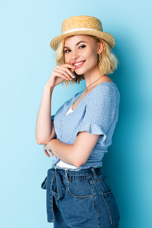 young woman in straw hat touching face and  on blue