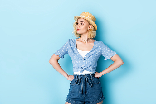 offended woman in straw hat standing with hands on hips on blue