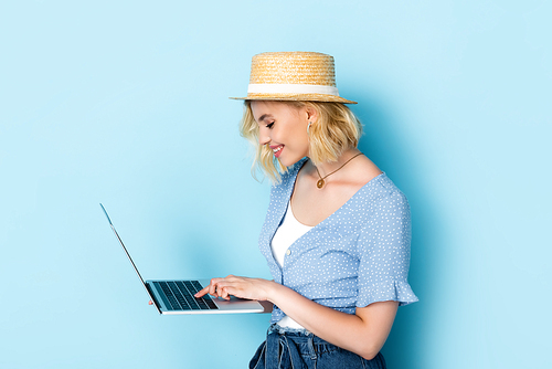 woman in straw hat standing using laptop on blue