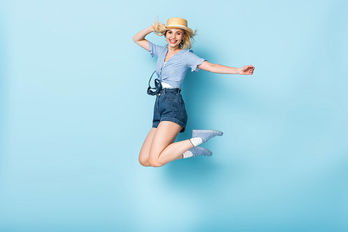 young woman in shorts and straw hat jumping on blue