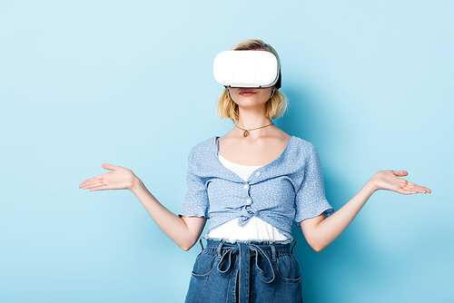 young woman in virtual reality headset gesturing on blue