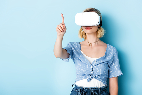 young woman in virtual reality headset pointing with finger on blue