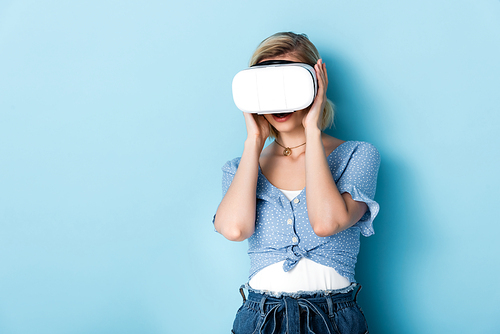 young woman touching virtual reality headset on blue