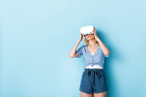 young woman touching virtual reality headset and standing on blue